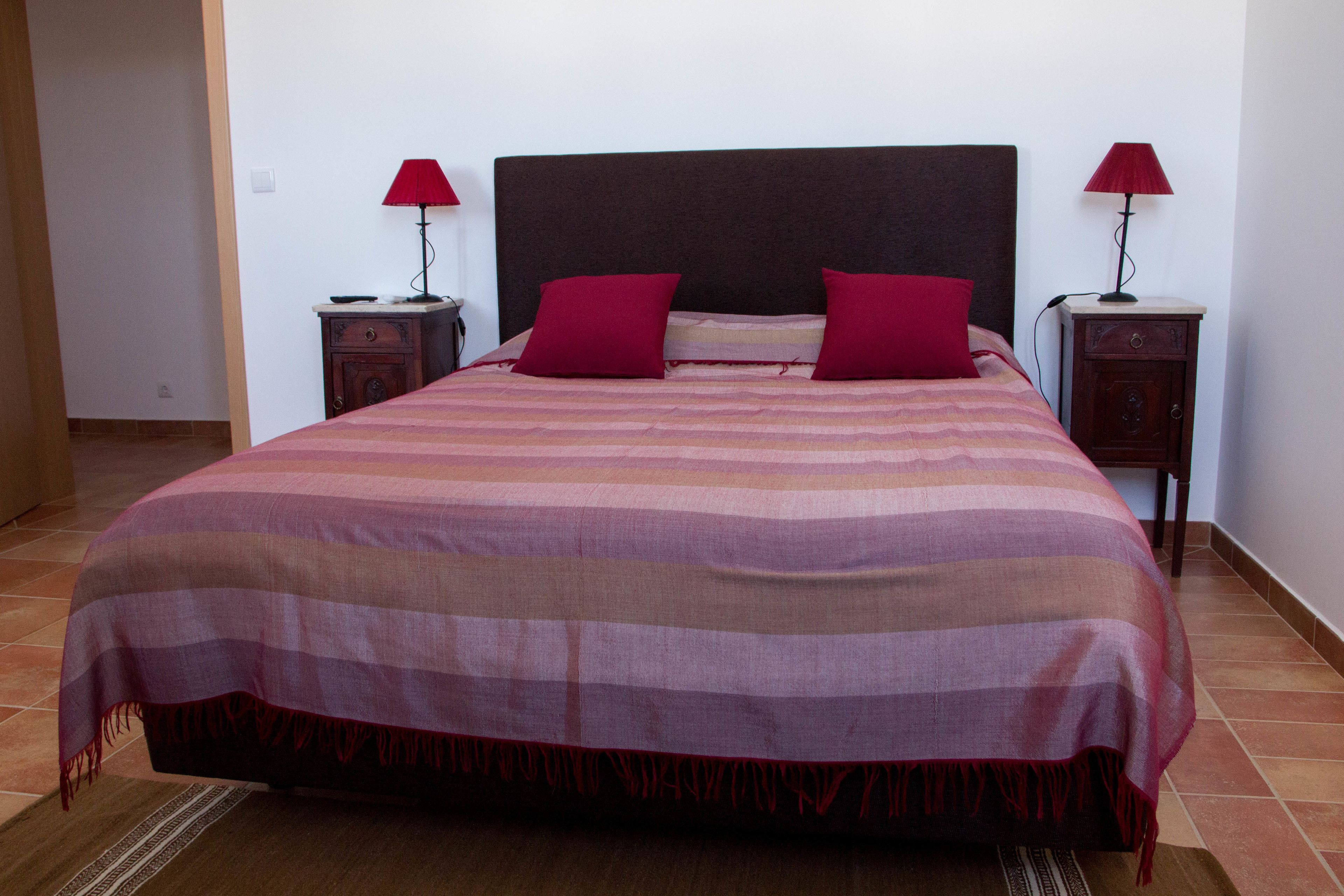 A neatly made bed with a striped bedspread and two red pillows, flanked by two bedside tables with lamps.
