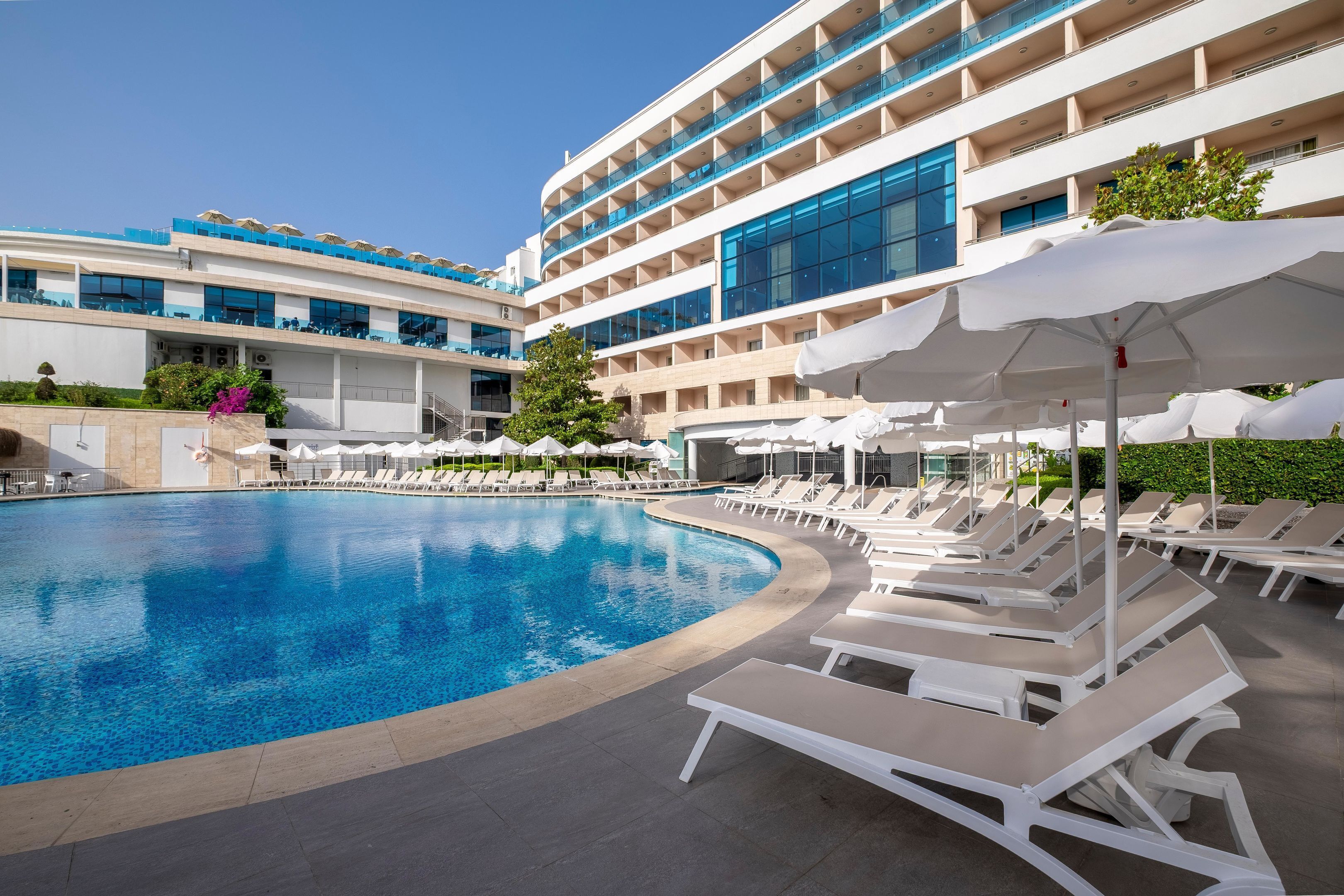 Un hôtel moderne doté d’une grande piscine, de chaises longues et d’un immeuble à plusieurs étages avec des balcons.
