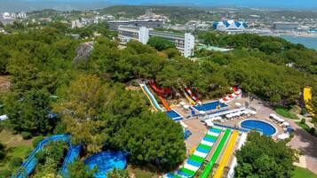 Parque acuático con múltiples toboganes y piscinas, rodeado de follaje y edificios al fondo.