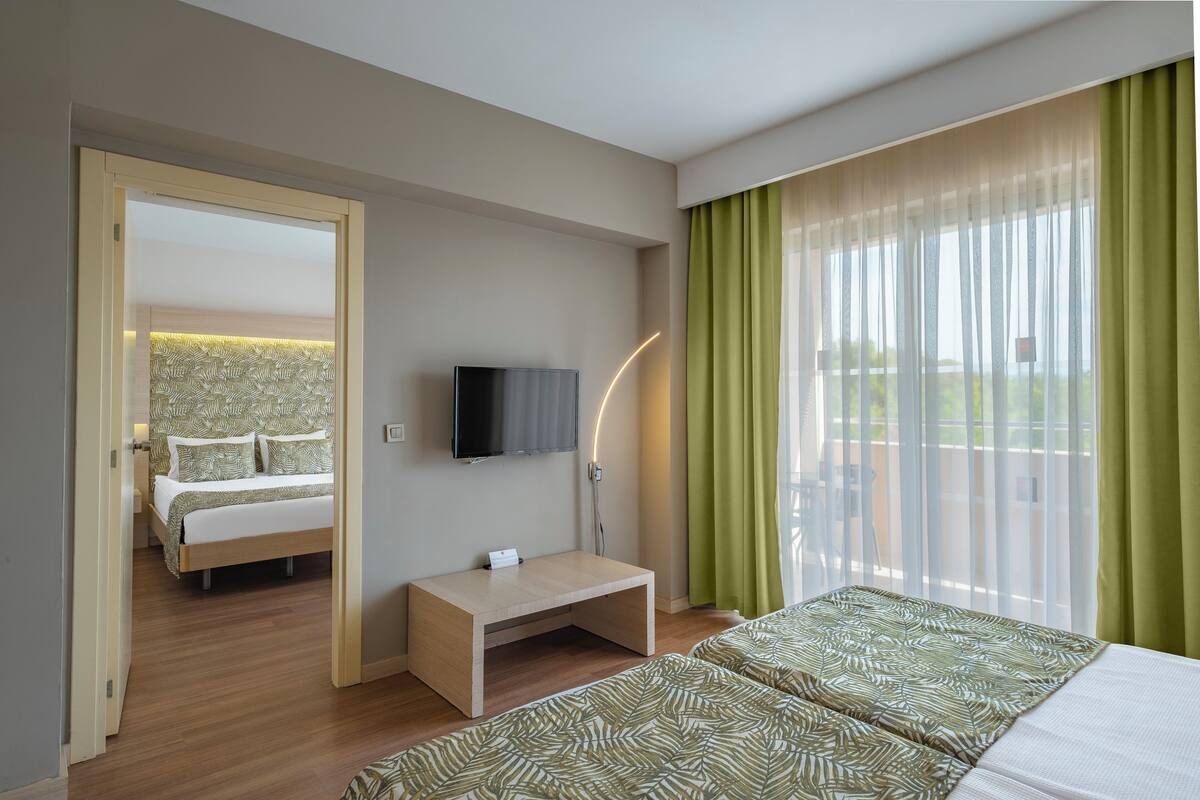 A hotel room with a bed, a desk, a TV, and a large window with curtains.