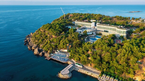 An aerial view of a coastal resort with a large building, a wind turbine, and a dock with a boat.