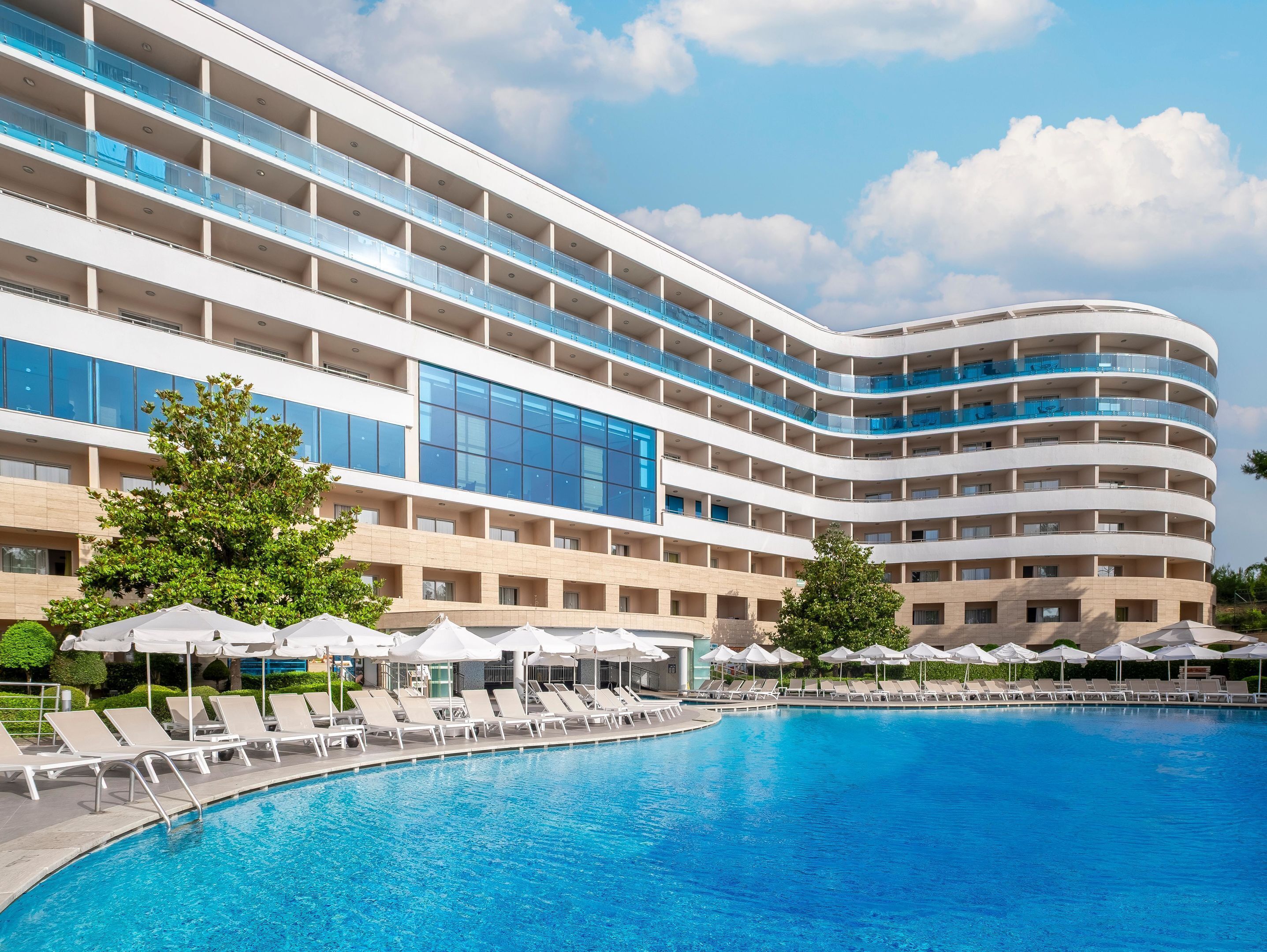 Un hotel moderno con una piscina grande, varios balcones y zonas de estar al aire libre.