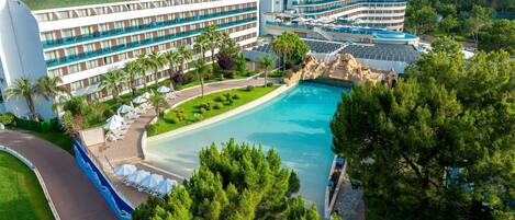 A hotel with a large pool, multiple balconies, and a view of the surrounding landscape.