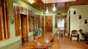 Uma área de refeições rústica com bancos de madeira e uma mesa comprida, paredes verdes e vigas de madeira no teto.