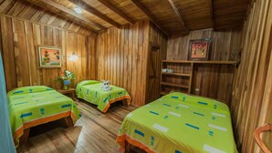 Quarto de madeira com duas camas, cada uma com roupa de cama verde e detalhes laranja. Apresenta paredes e teto de madeira.