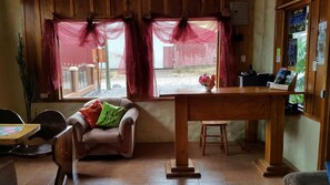 Ein gemütliches Zimmer mit einem Holztisch, einem gepolsterten Sessel und einem Fenster mit transparenten Vorhängen.