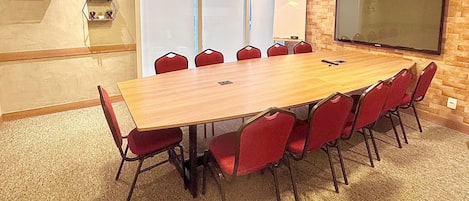 Un salón de conferencias con una gran mesa de madera, sillas rojas, una pizarra y un televisor en la pared.