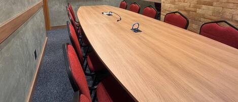 Un salón de conferencias con una larga mesa de madera, sillas tapizadas en rojo, un televisor de pantalla plana montado en la pared e iluminación empotrada en el techo.