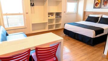 Une chambre à coucher avec un lit, un bureau et une chaise. On y trouve un placard avec des étagères et une fenêtre.