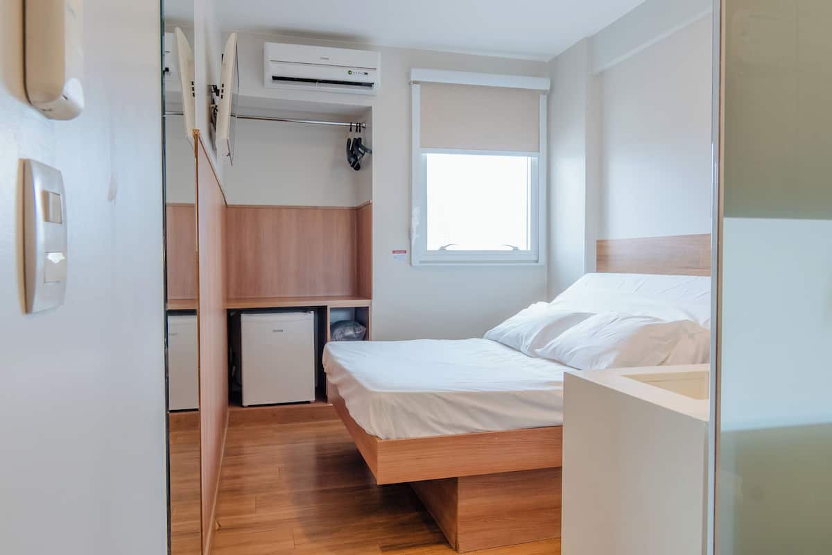 Una habitación compacta con cama, una kitchenette pequeña y una ventana.