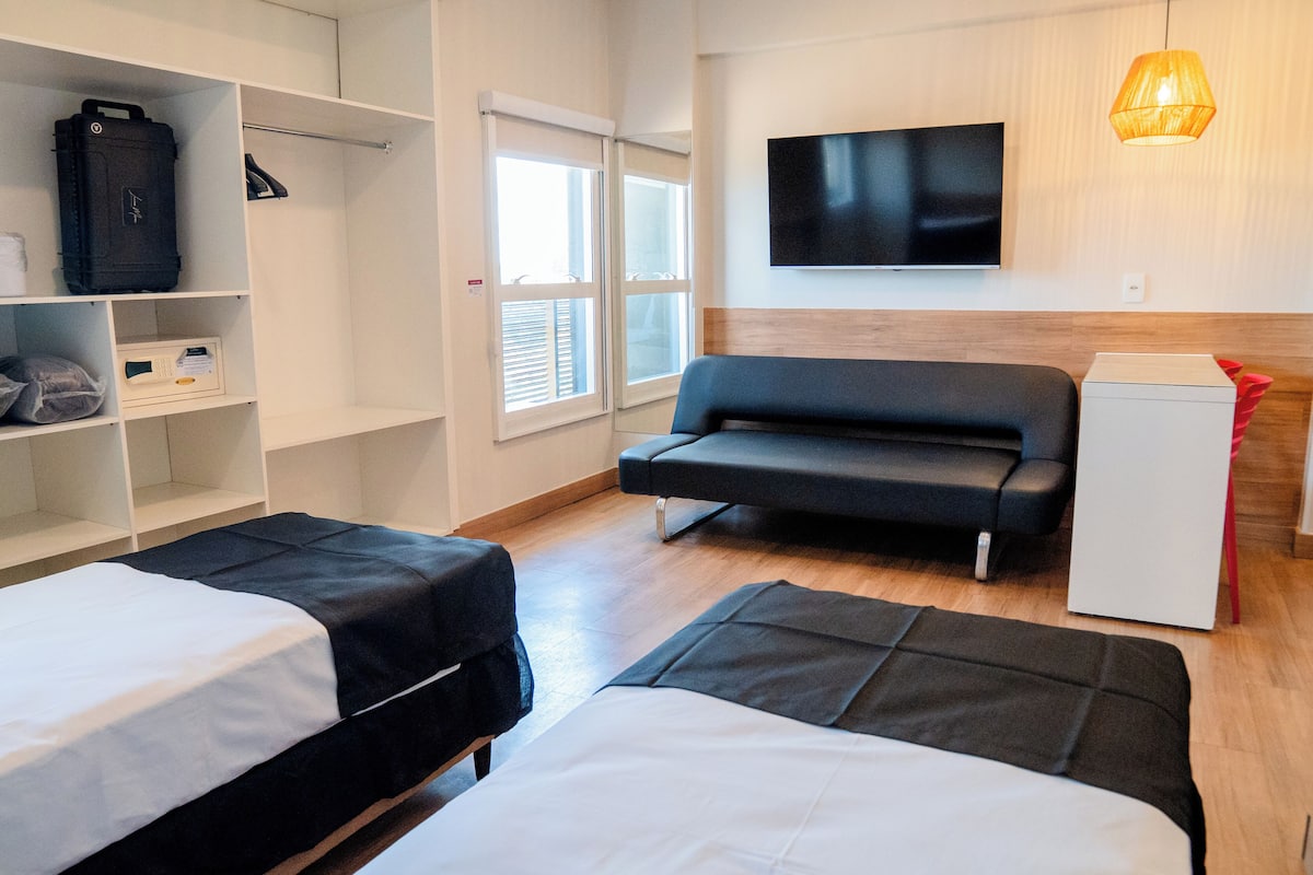 Una habitación de hotel con dos camas, un sofá, un televisor y un armario.