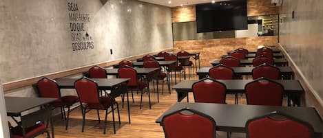 A conference room with tables and chairs, a wooden accent wall, and a flat-screen TV mounted on the wall.
