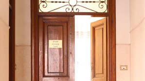 Une porte en bois, sur laquelle est apposée une plaque indiquant « Prati Luxury Suite », donne sur un couloir carrelé.