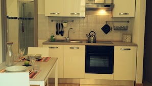 Une cuisine moderne avec des armoires blanches, un four encastré, une hotte de cuisinière en acier inoxydable et une cabine de douche en verre.