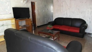 Una sala de estar con un sofá de cuero negro, una mesa de centro de madera y un televisor de pantalla plana sobre un mueble de madera.