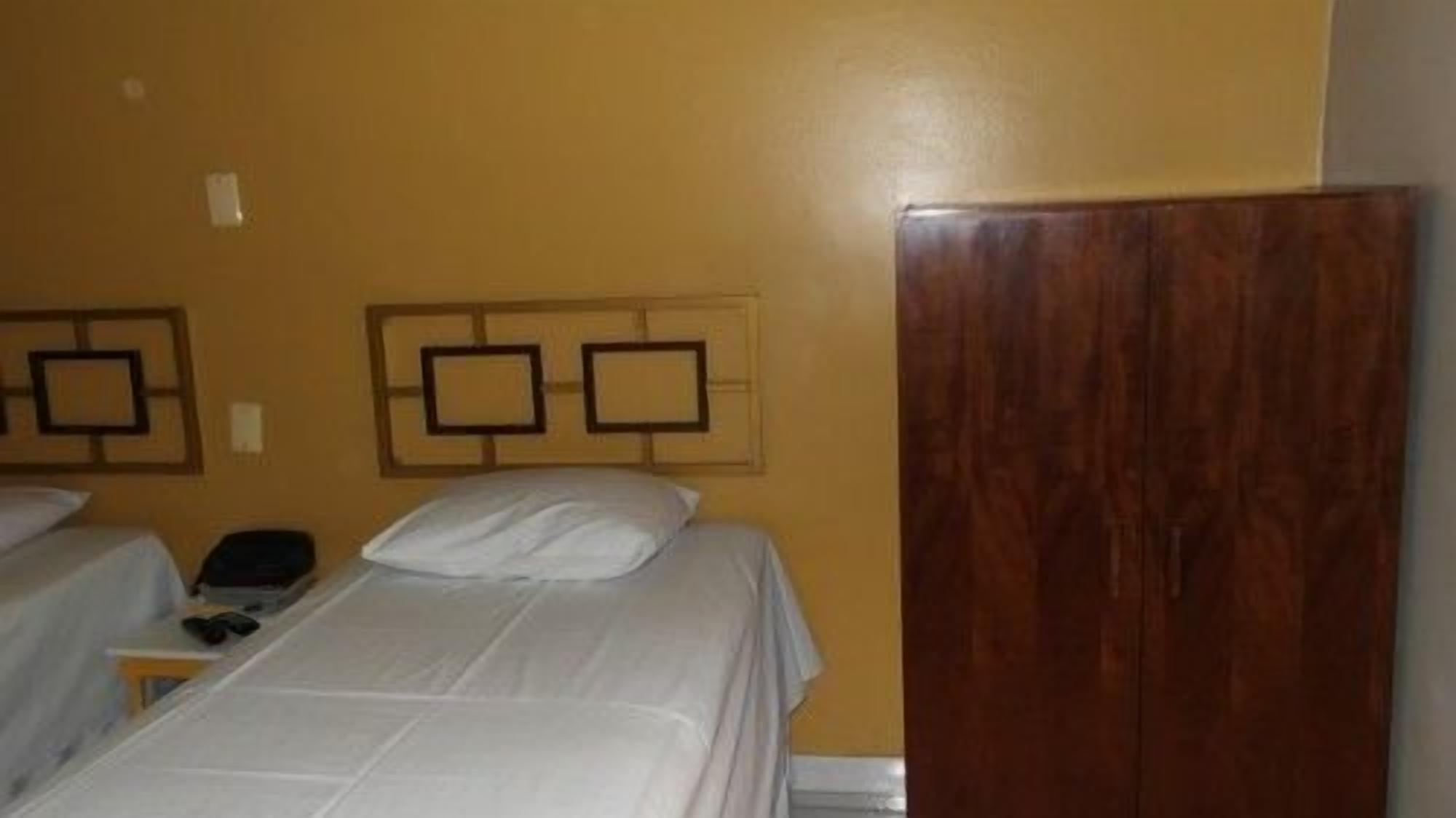 A hotel room with two beds, a wooden wardrobe, and a wall-mounted TV.