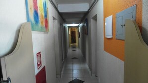 Un pasillo estrecho con suelo de baldosas, un cuadro abstracto colorido a la izquierda y una puerta con un letrero rojo a la derecha.