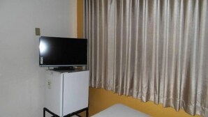 Una habitación con una televisión sobre un mueble blanco pequeño, cortinas beige y una pared amarilla.