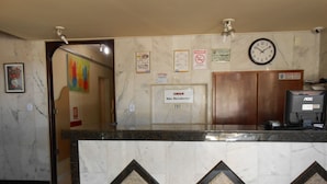 Zona de recepción de un hotel con mostrador de mármol, un reloj y varios carteles, incluyendo un letrero de no fumar y un aviso de registro.