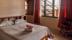A bedroom with a wooden ceiling, a bed with a patterned bedspread, a chair, and a window with curtains. - Hotel El Atardecer (Monteverde)