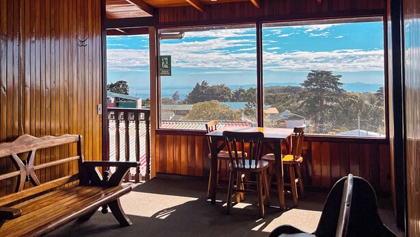 A wooden cabin with a dining area and a large window offering a scenic view. - Hotel El Atardecer (Monteverde)