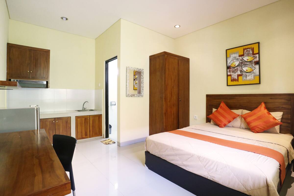 A hotel room with a bed, a wooden wardrobe, a dining table, and a kitchenette.