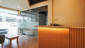 A reception area with a wooden reception desk, a glass partition, and a view of a car outside. - Dee Mansion Bali (Denpasar)