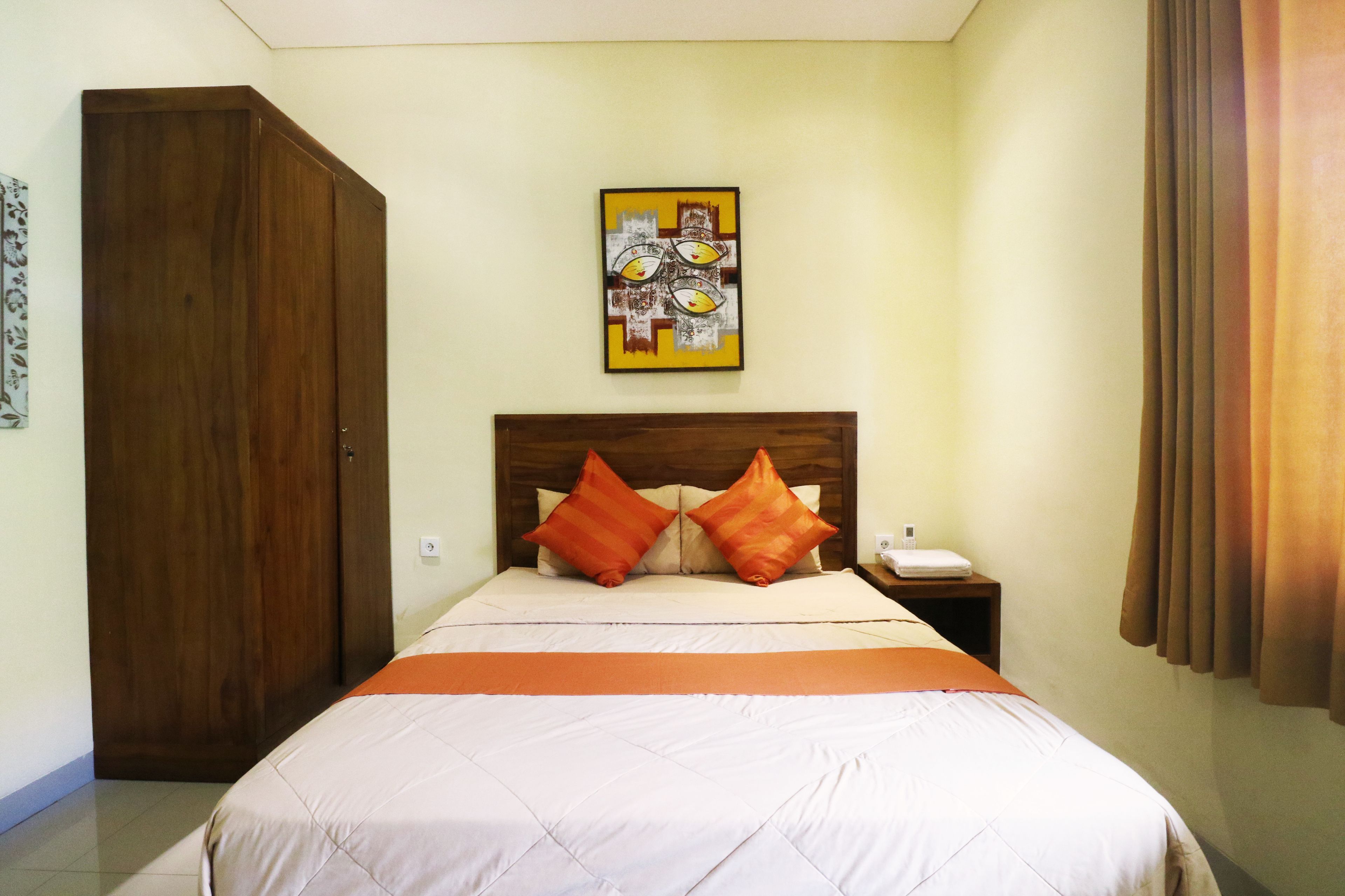 A bedroom with a bed, a wooden wardrobe, a nightstand, a wall-mounted painting, and a curtain.