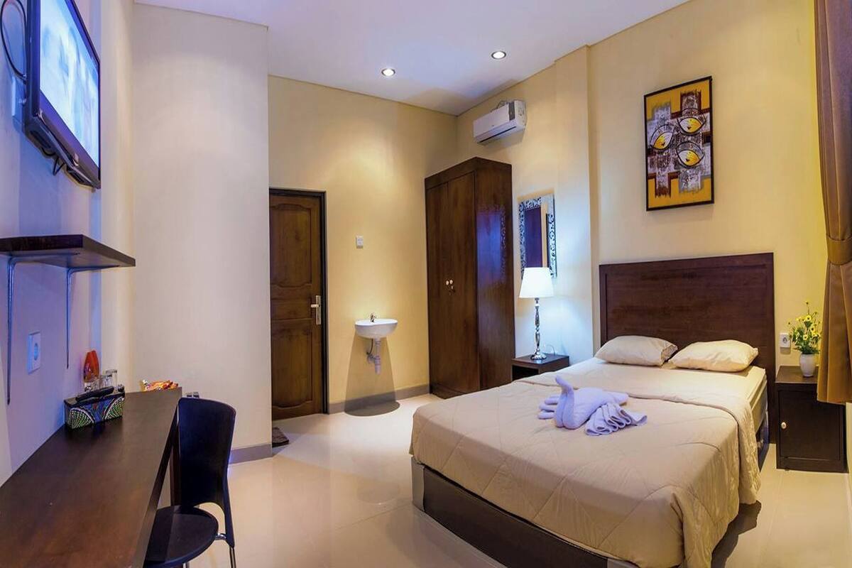 A hotel room with a bed, bedside table, lamp, and a painting on the wall.