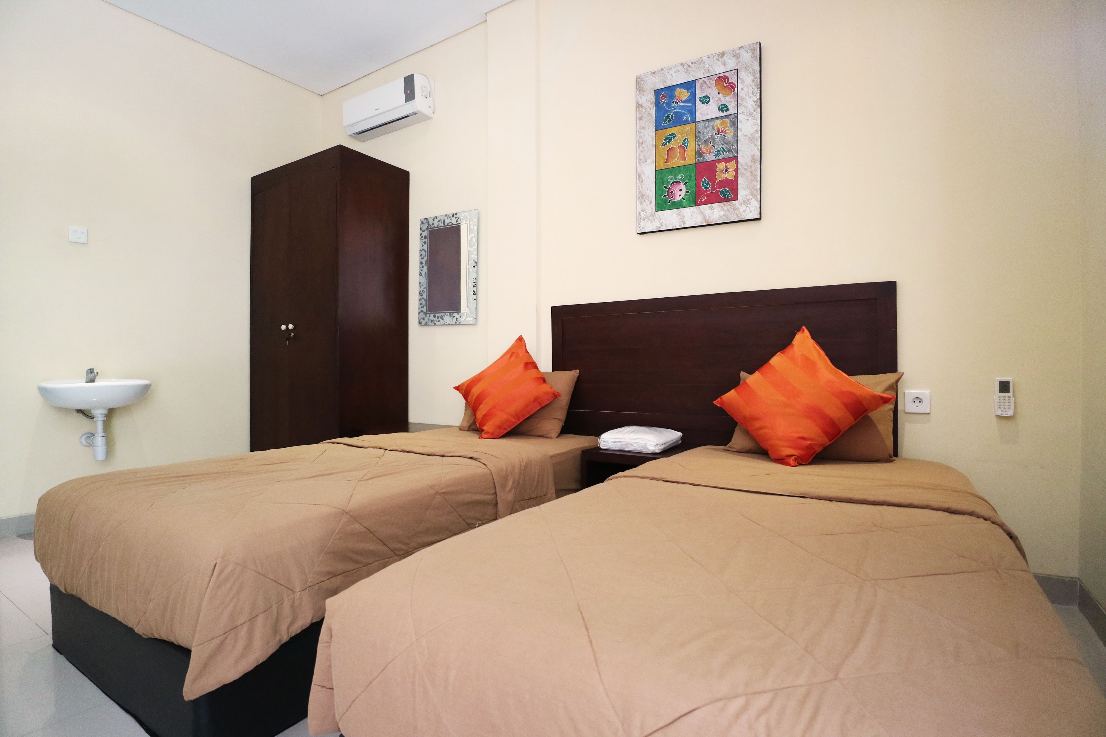 A hotel room with two beds, a nightstand, a wall-mounted air conditioner, a wall-mounted artwork, and a sink.