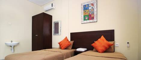 A hotel room with two beds, a nightstand, a wall-mounted air conditioner, a wall-mounted artwork, and a sink.