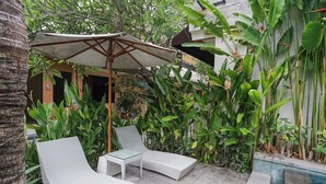 A patio area with two white lounge chairs, a glass-top table, and a large umbrella. - Dee Mansion Bali (Denpasar)