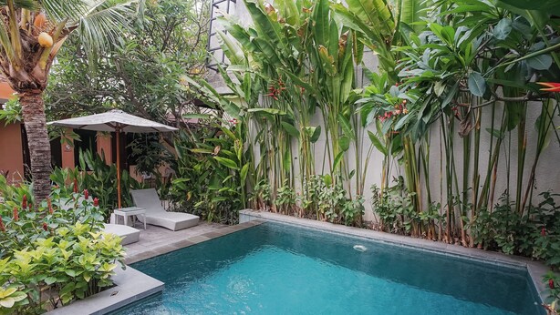 A rectangular swimming pool surrounded by lush greenery and a white wall. - Dee Mansion Bali (Denpasar)