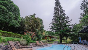 Un área de piscina con sillones de descanso y un edificio pequeño al fondo.