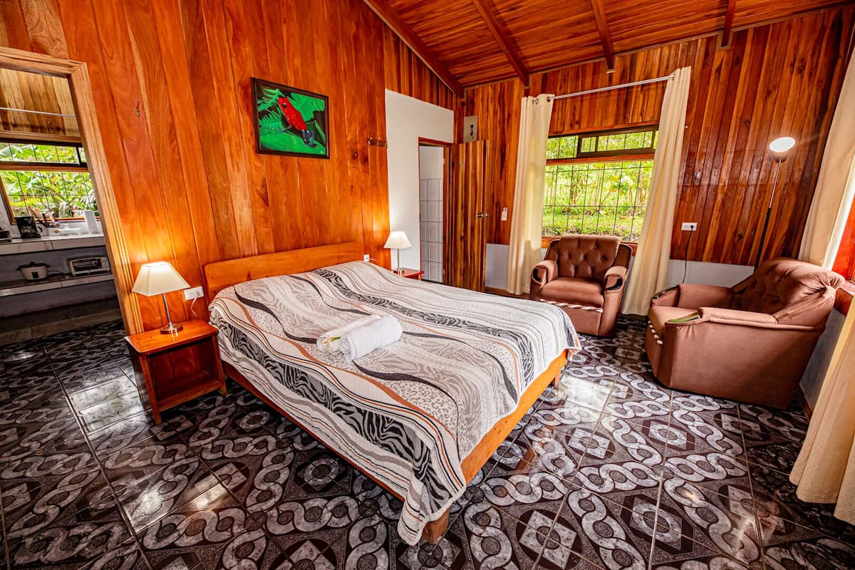 A wooden-paneled room with a bed, a chair, and a painting on the wall.