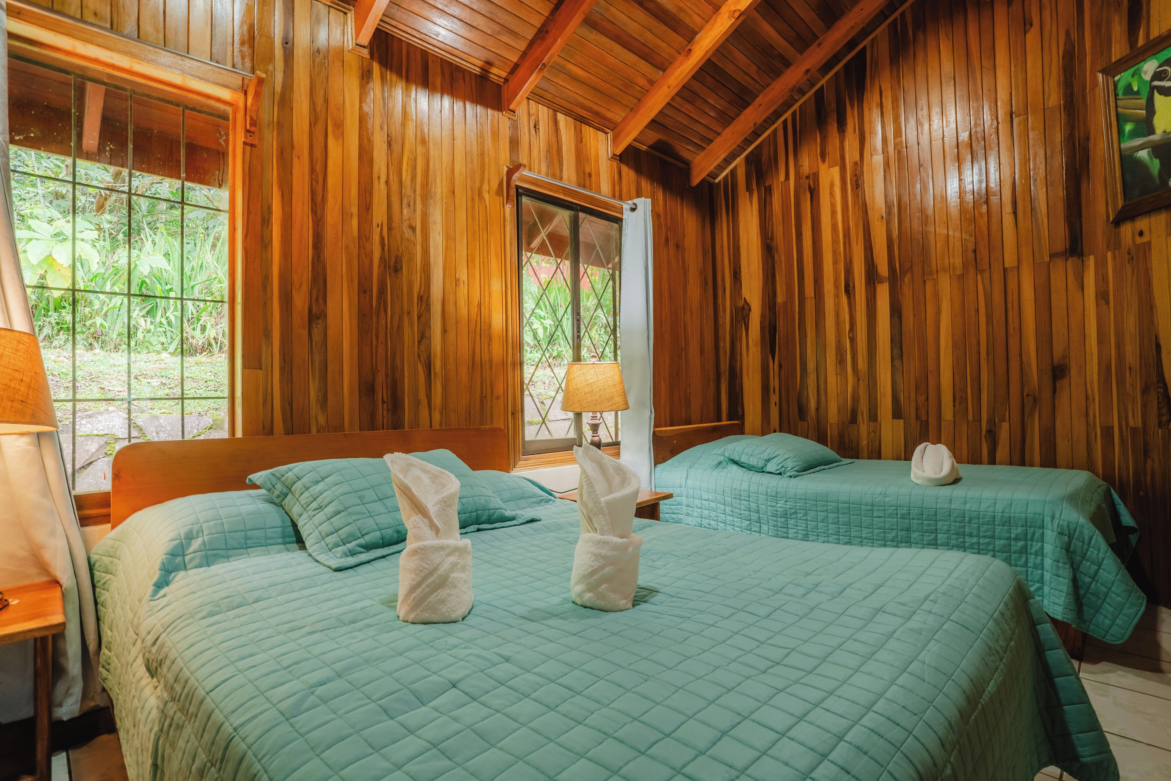 A wooden room with two beds, each with a green quilt and towels.