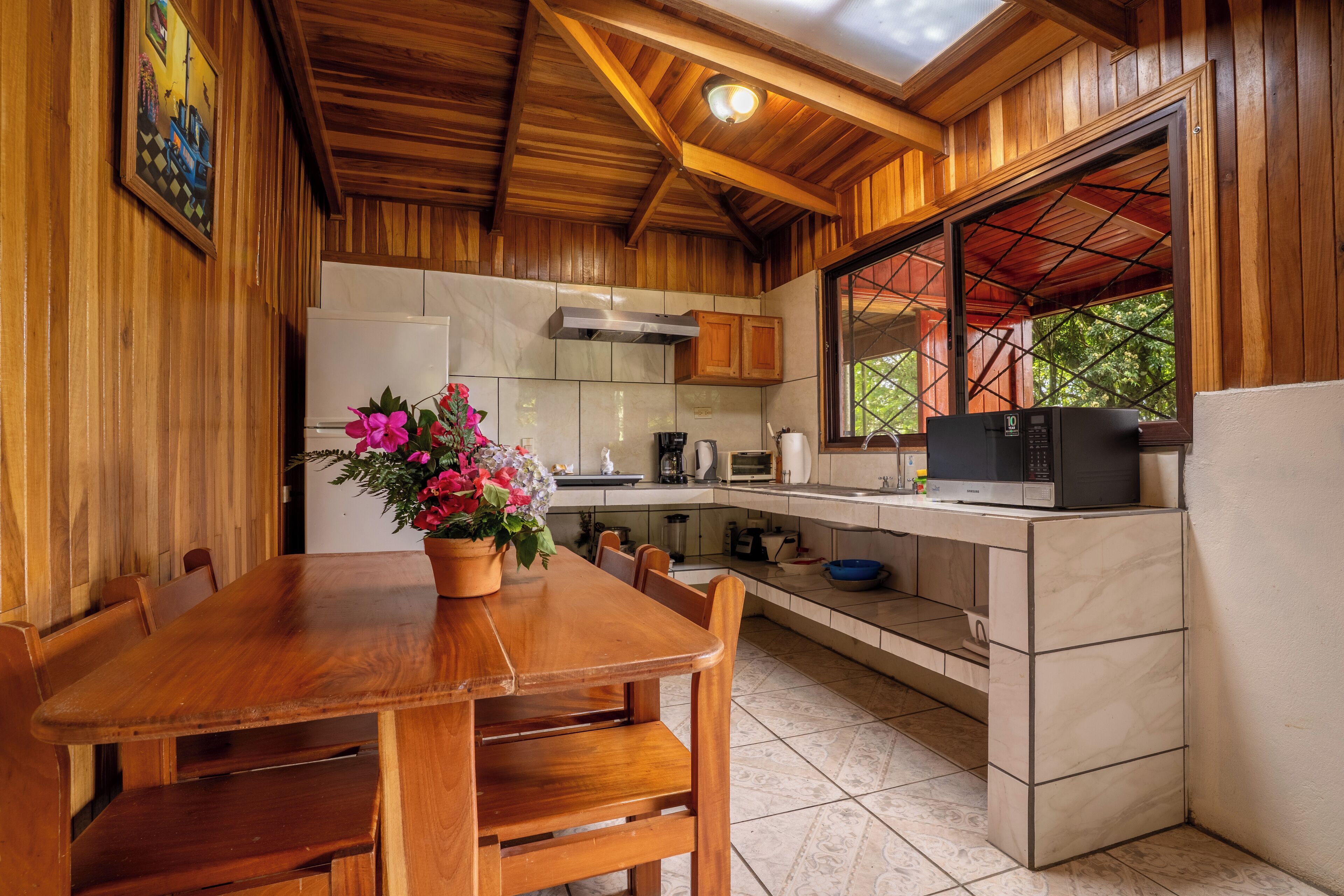 A wooden interior with a dining table, chairs, a kitchen area, and a window with a view.