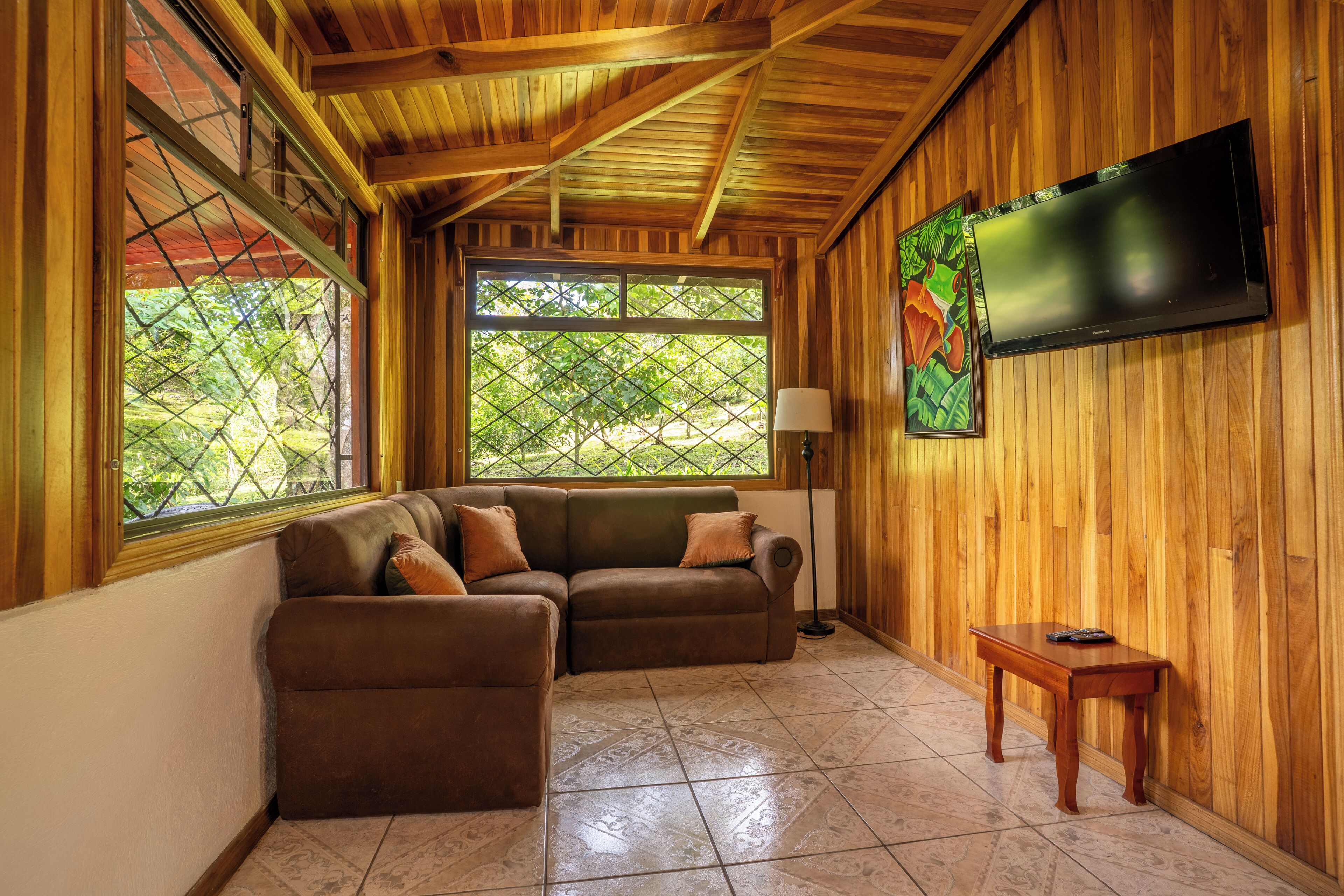 A wooden-paneled room with a sectional sofa, a flat-screen TV, and a small table.