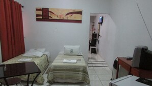 Une petite chambre d’hôtel avec deux lits simples, un bureau avec une chaise, une télévision et un tableau au mur.