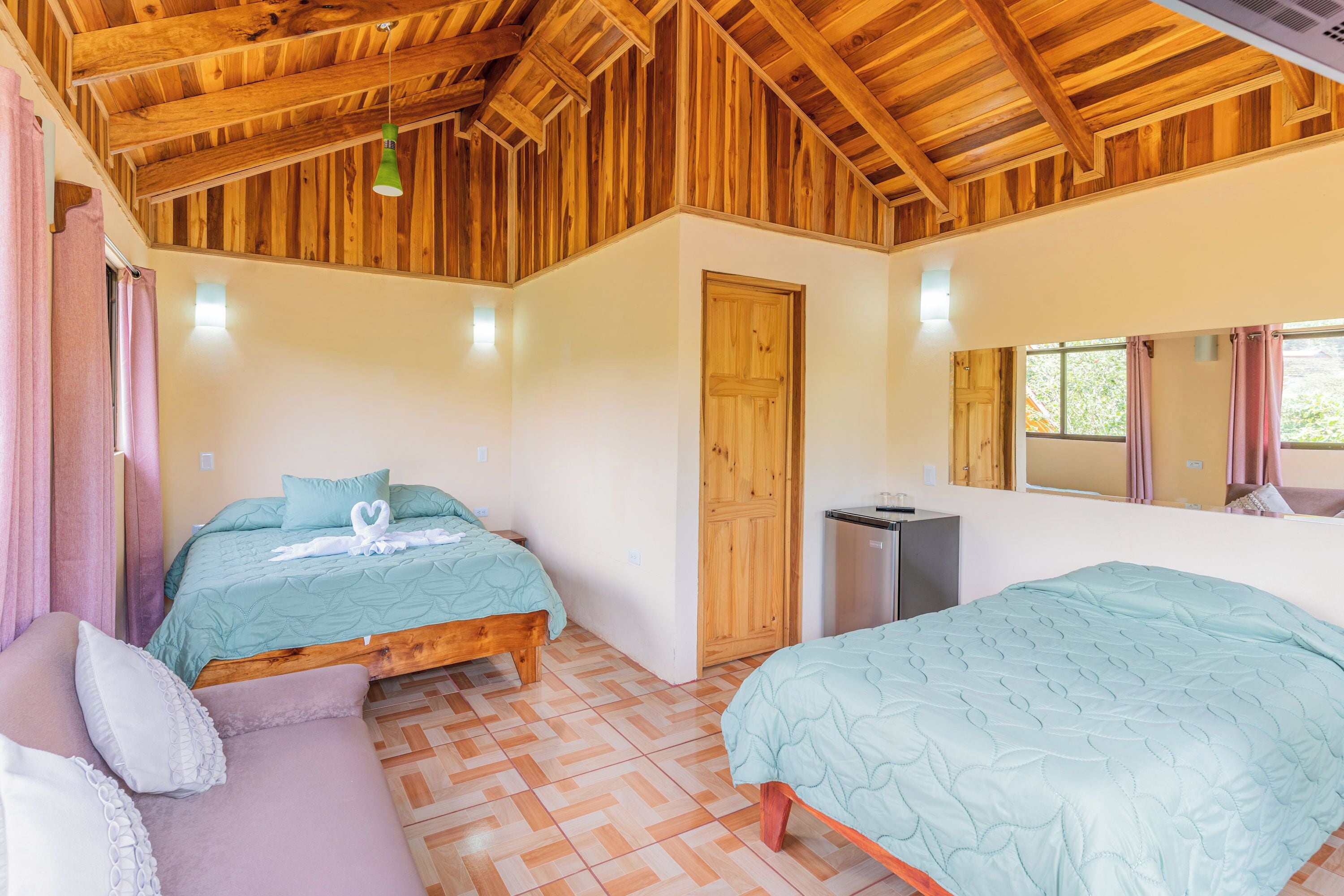 Un dormitorio con dos camas, techo de madera, un escritorio pequeño y un espejo.