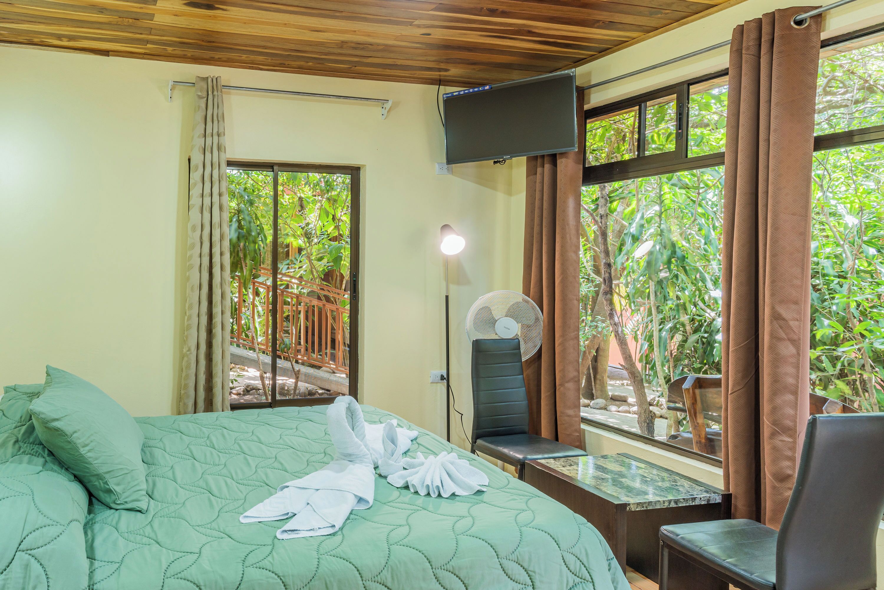 A hotel room with a bed, a desk, a chair, a TV, and a window with curtains.