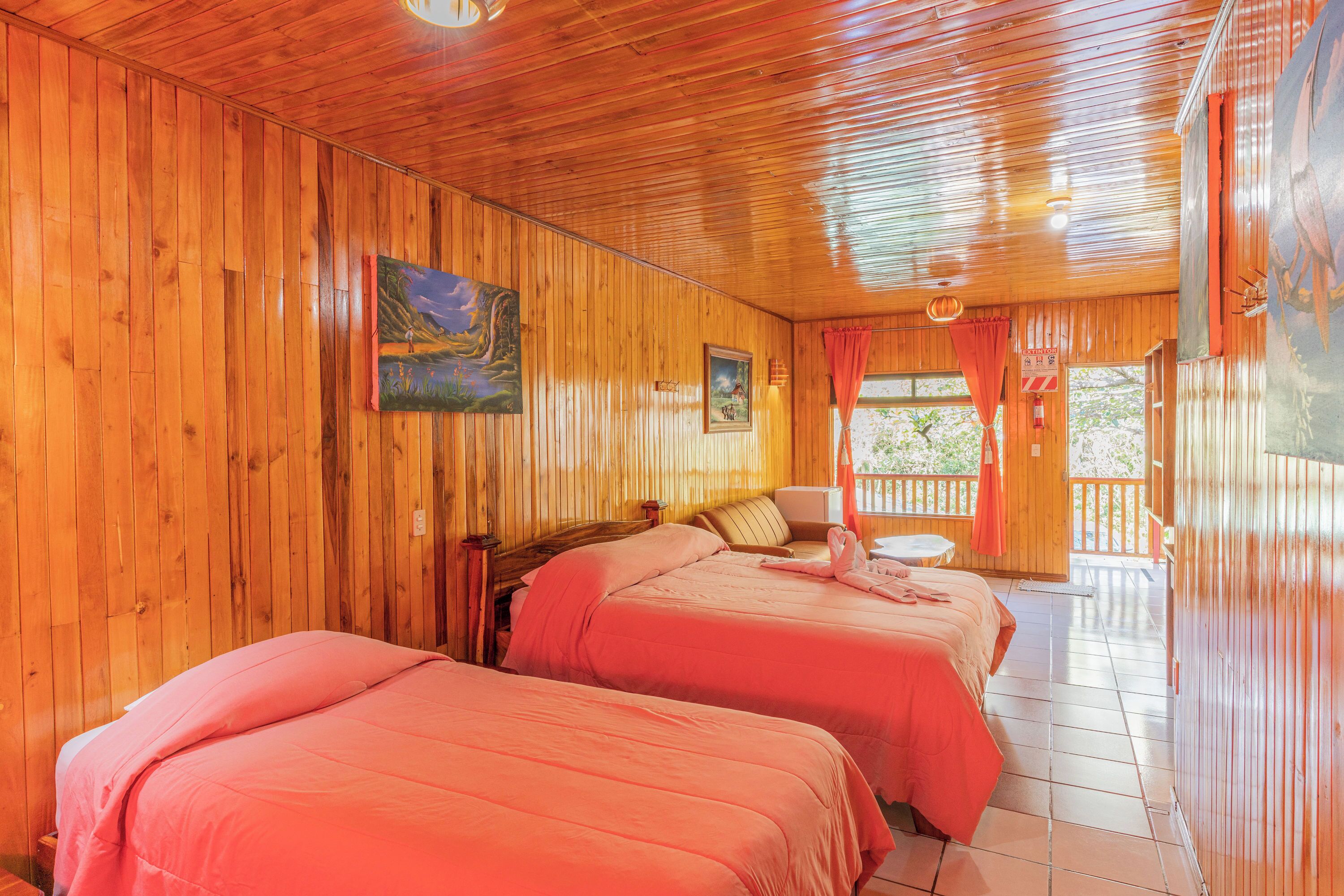 A wooden cabin with two beds, a painting, and a balcony with a red curtain.