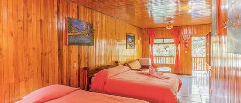 A wooden cabin with two beds, a painting, and a balcony with a red curtain.