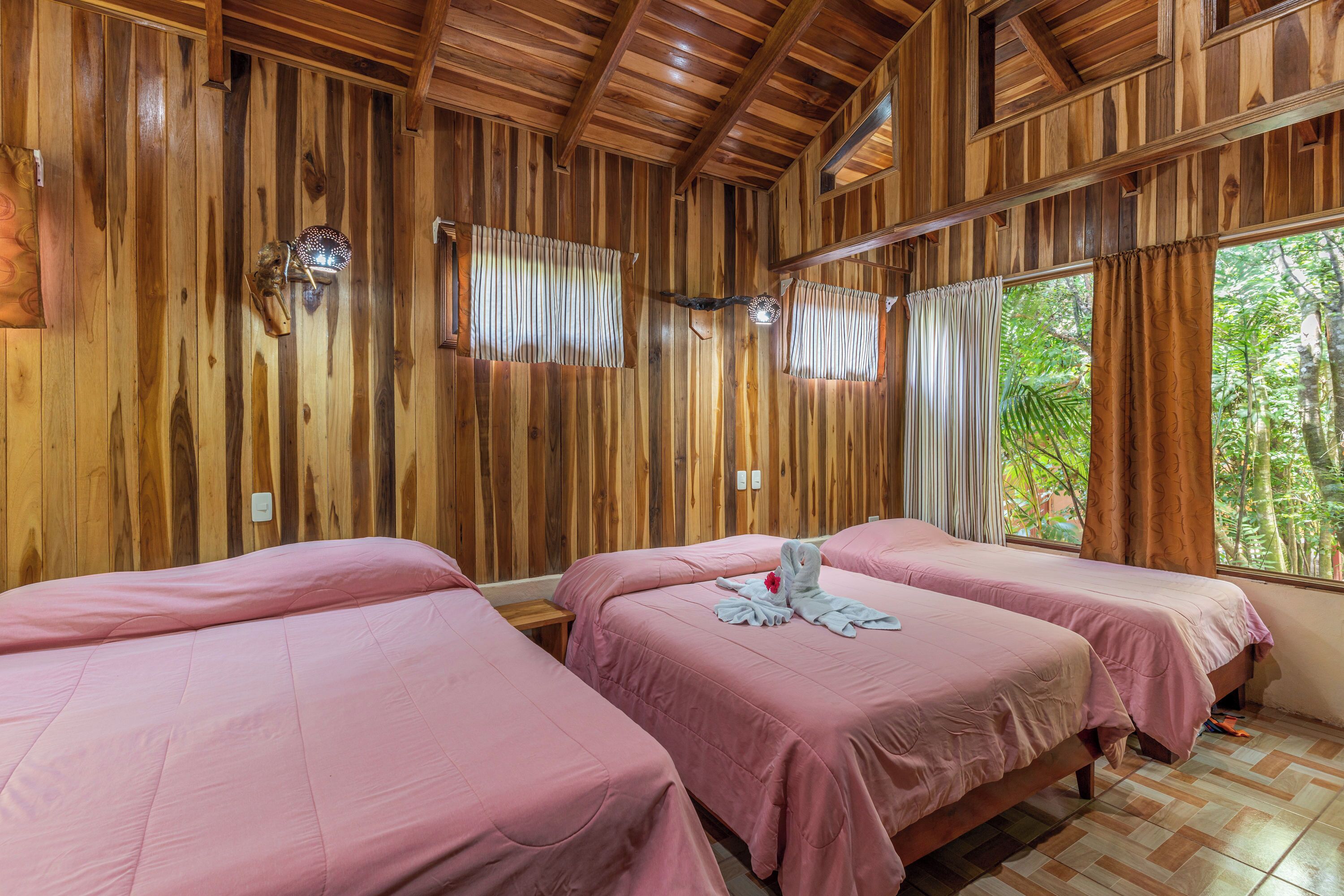 A room with wooden walls and two beds with pink bedding.