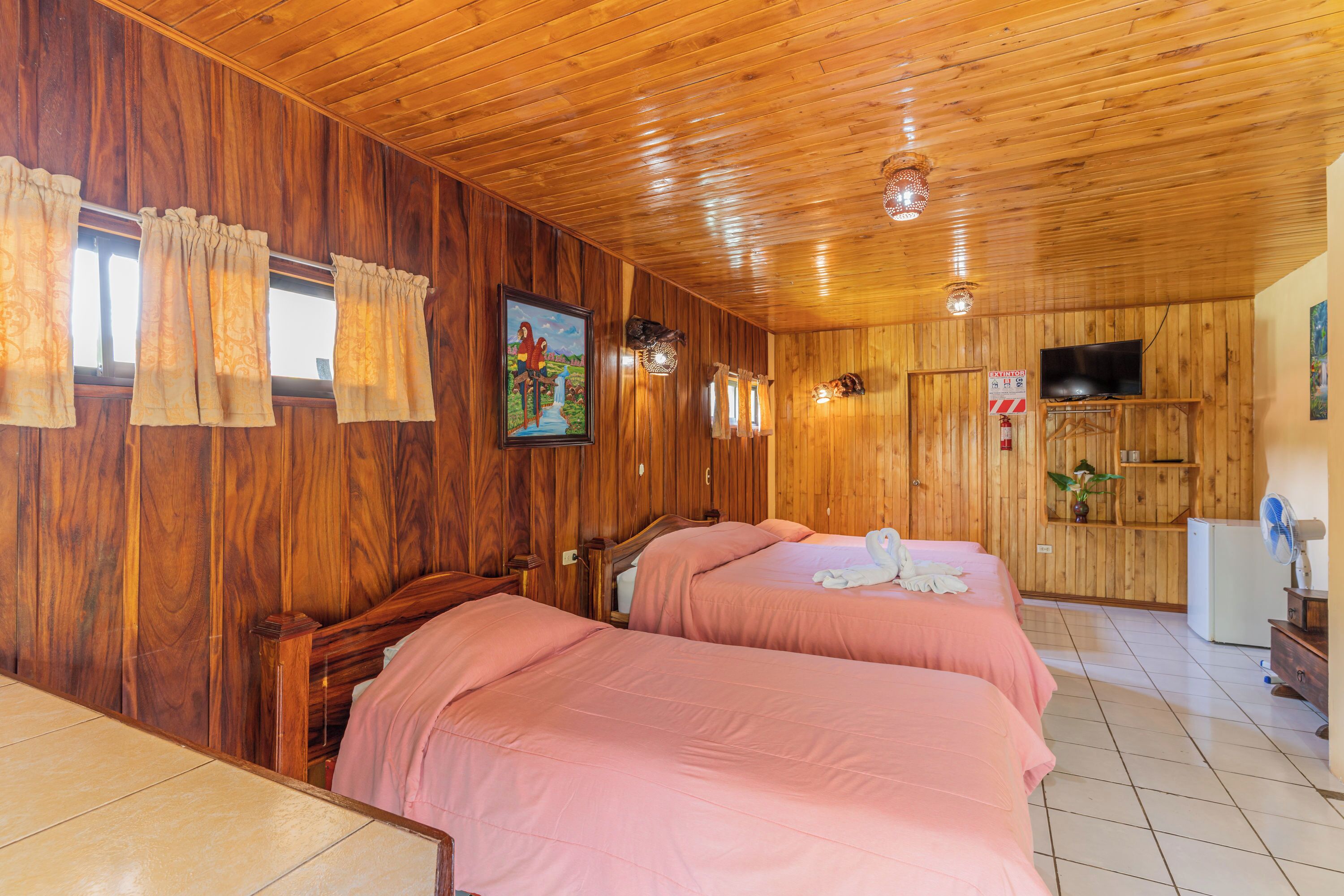 A wooden-paneled room with two beds, a television, and a refrigerator.