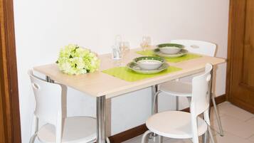 Un comedor con una mesa dispuesta para dos personas, sillas blancas y un mantel individual verde.