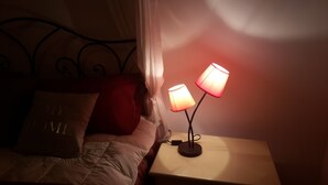A bed with a white comforter and a pillow with "TOM" on it. There is a nightstand with a lamp and a small table beside it. - Le Dimore del Sole (Cagliari)