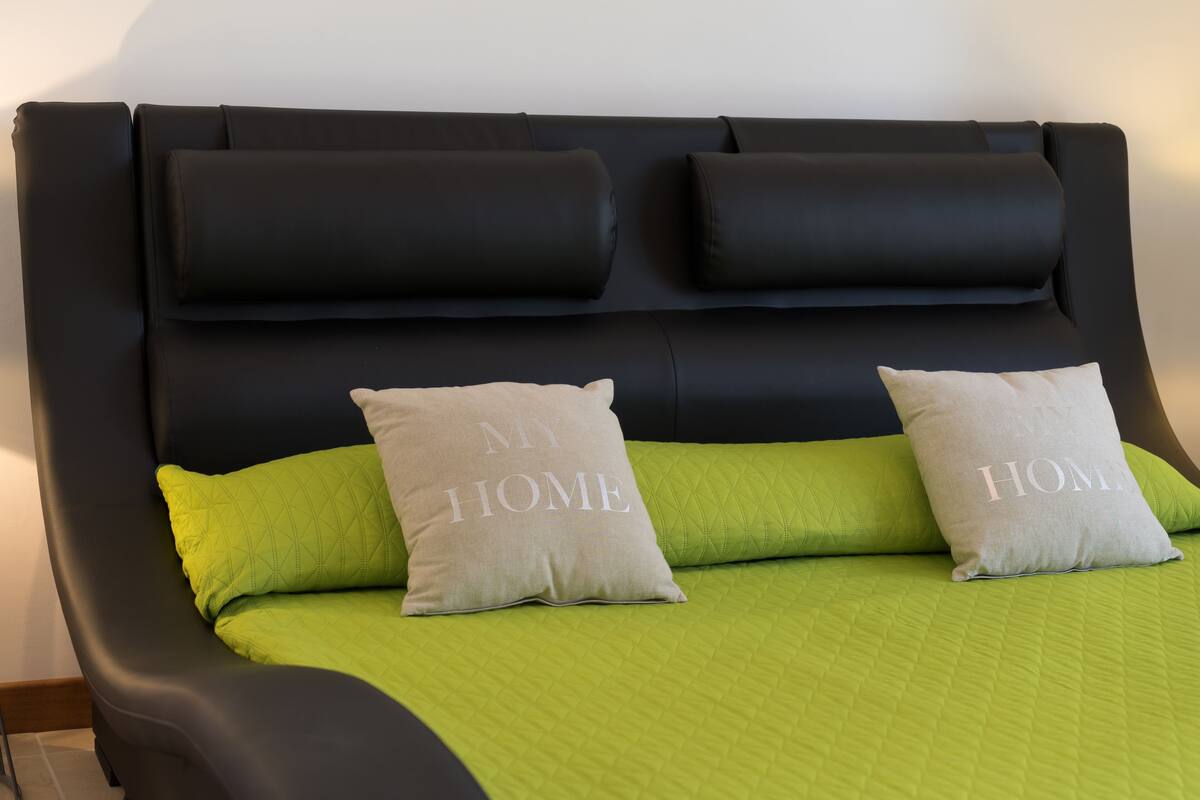 A bed with a green quilt and two pillows, one with "MY HOME" text.
