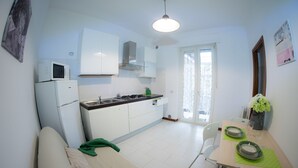 A compact kitchen with white cabinets, a microwave, and a stove. There is a dining table with chairs and a green placemat. - Le Dimore del Sole (Cagliari)