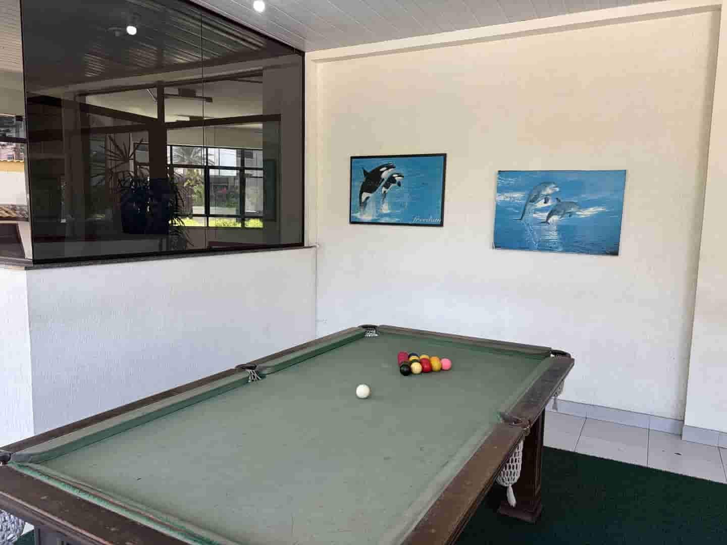A pool table with balls, a window with a view, and two framed pictures on the wall.